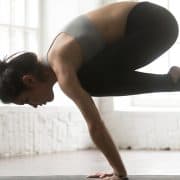 women in a yoga pose on a mat in studio kakasana bakasana meaning