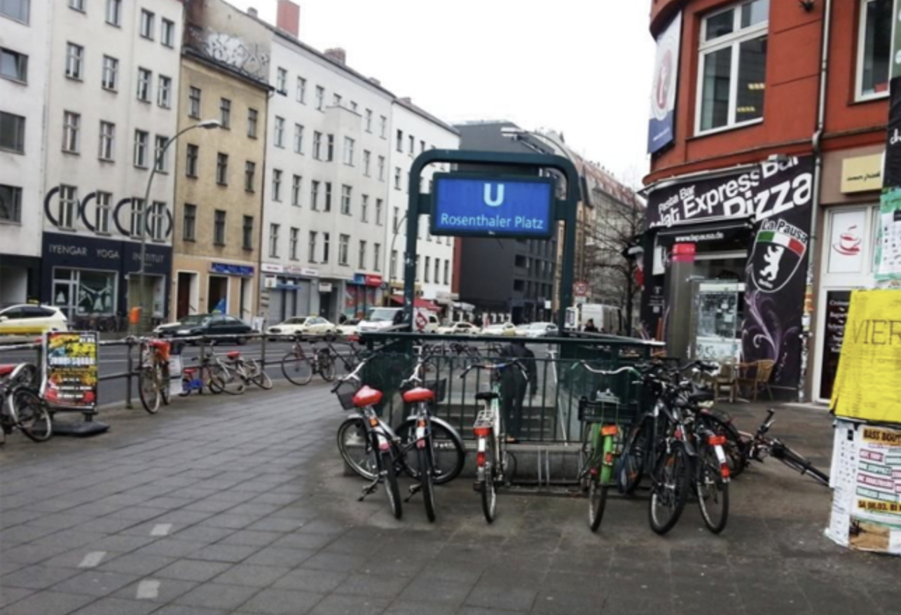 Rosenthaler Platz in Berlin Mitte with bicycles parked near the U-Bahn entrance and surrounding shops on a typical city street.