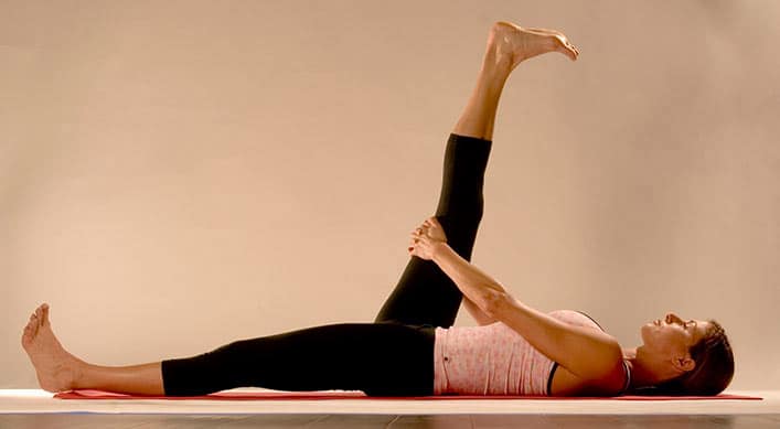 woman on floor on yoga mat supta padangusthasana (Reclined Leg Stretch)
