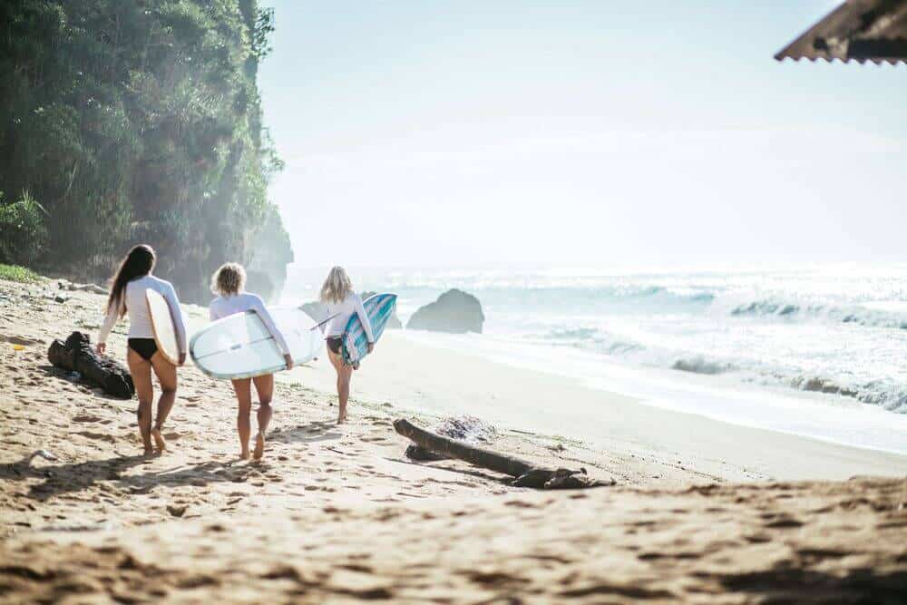 three women walking on beach with surf boards bali all inclusive ubud healing meditation spa nudes Indonesia woman for couples resort surf and surfing vacation canggu