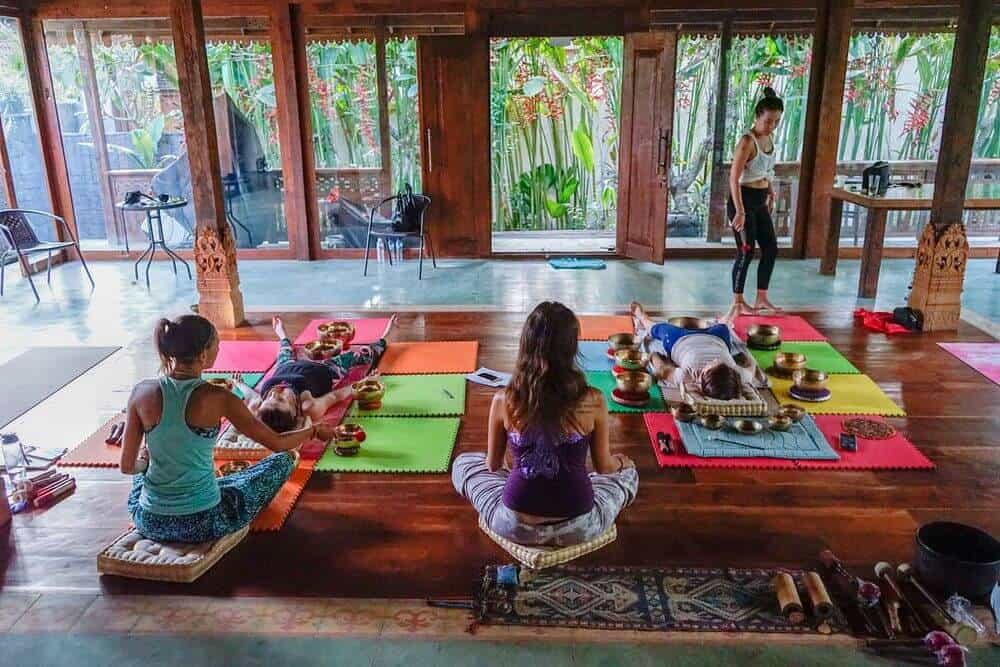 3 women in wooden house 2 laying on floor three women walking on beach with surf boards bali yoga all inclusive ubud healing meditation spa nudes Indonesia woman for couples resort surf and surfing vacation canggu sound healing