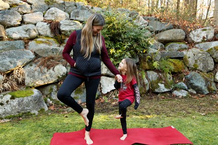Mother and daughter practicing partner tree pose outdoors, showing how regular yoga practice brings balance to family daily life