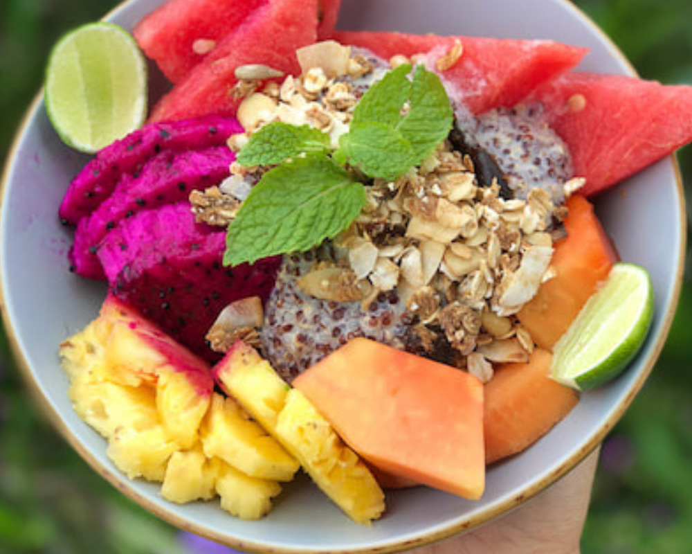 Colorful tropical fruit bowl with chia pudding, granola, fresh pineapple, watermelon, dragon fruit, papaya, and lime wedges