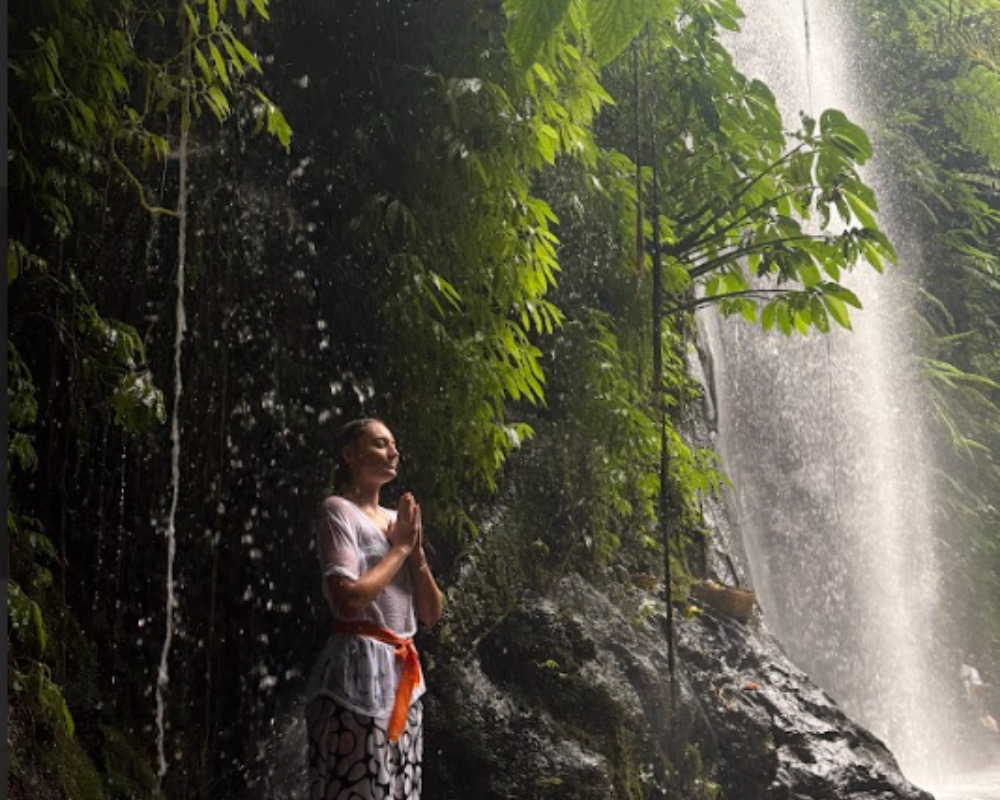 Yoga student in traditional attire meditating under a sacred Balinese waterfall.