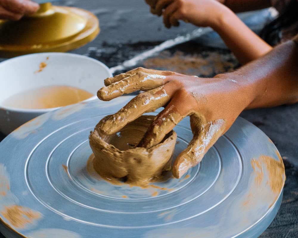 Hands shaping clay on a pottery wheel, with a bowl of water beside it, demonstrating the pottery-making process