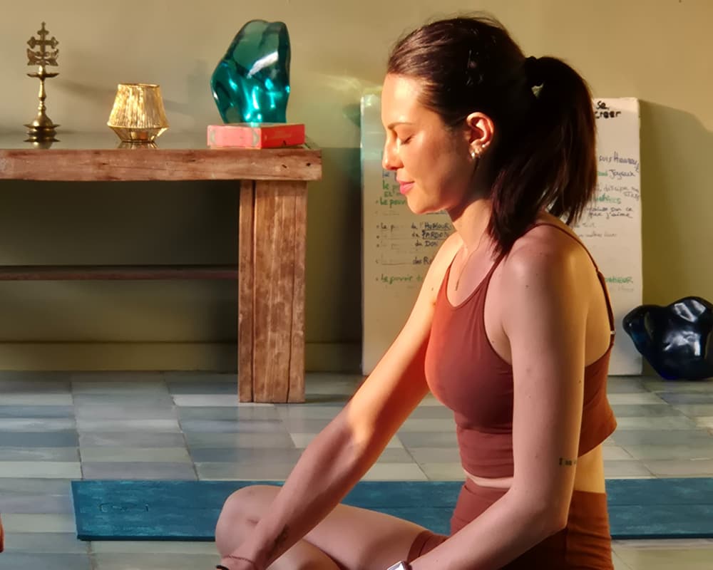 Woman in a yoga studio sitting in a calm meditative pose, bathed in warm sunlight, with serene expression