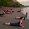 A group performs yoga poses on a serene Bali beachfront at sunrise or sunset, illustrating an ideal outdoor studio setting for a yoga retreat