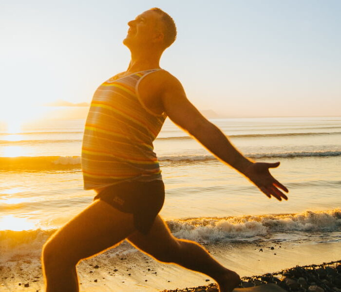 A man in Warrior 1 pose on a sunny beach at sunrise, showcasing ideal beachfront yoga locations for a Bali retreat