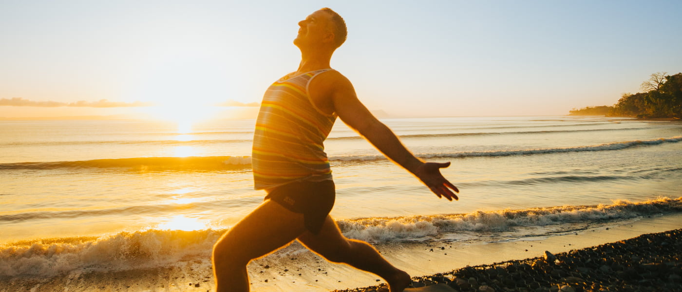A man in Warrior 1 pose on a sunny beach at sunrise, showcasing ideal beachfront yoga locations for a Bali retreat