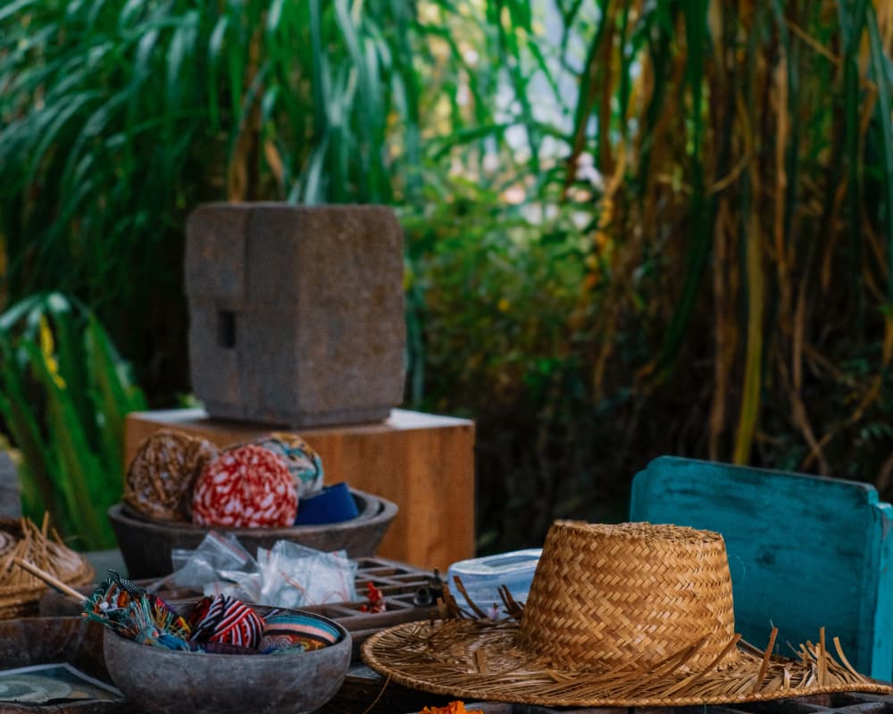 close-up of a creative workspace with straw hats and colorful fabrics, surrounded by lush greenery outside