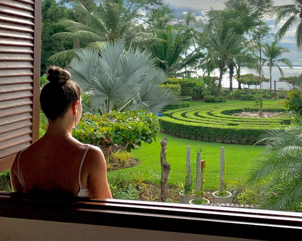 Woman overlooks tropical garden, representing Bali retreat's serene landscape for reset.