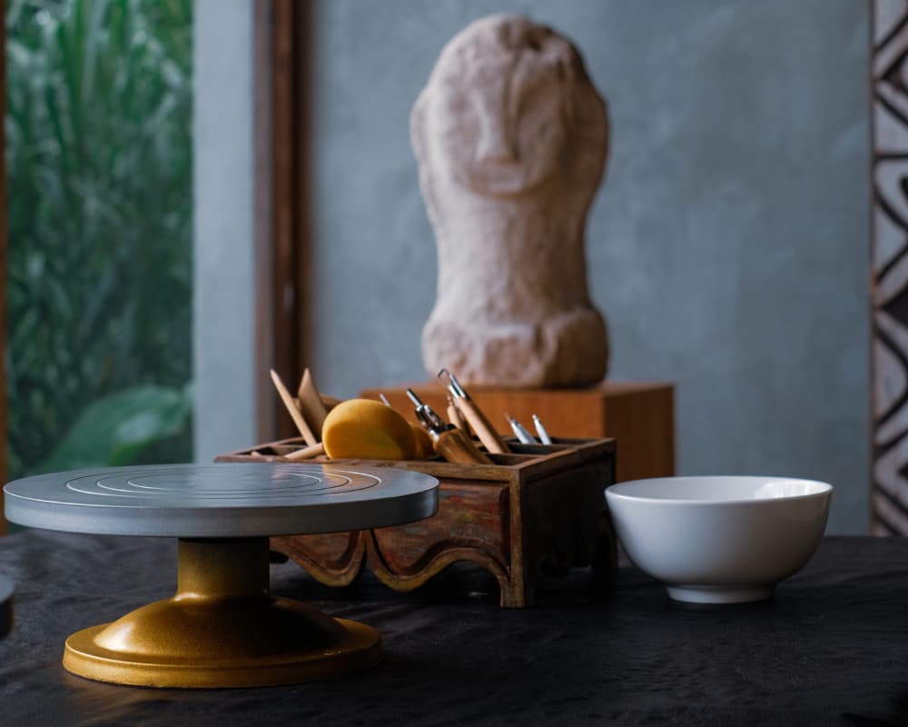 Artisan pottery workspace featuring a rotating wheel, tools, and a stone sculpture in the background