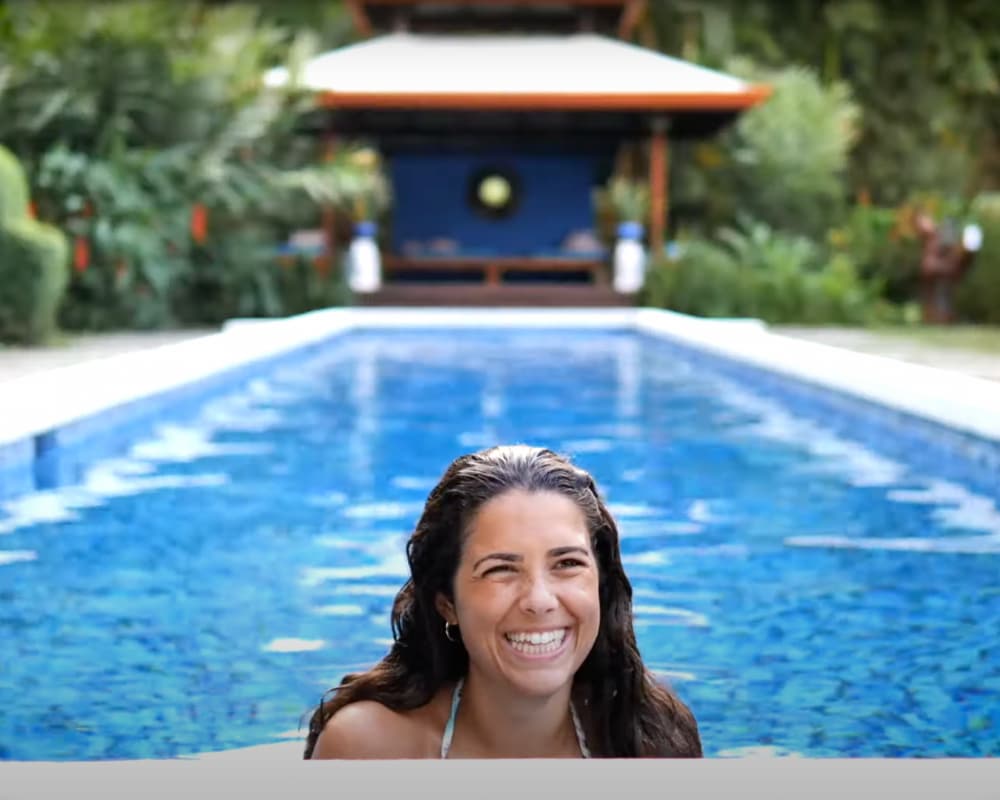 A smiling woman emerges from a refreshing swimming pool, highlighting the luxurious amenities and serene settings often found at Bali yoga retreat villas and spas