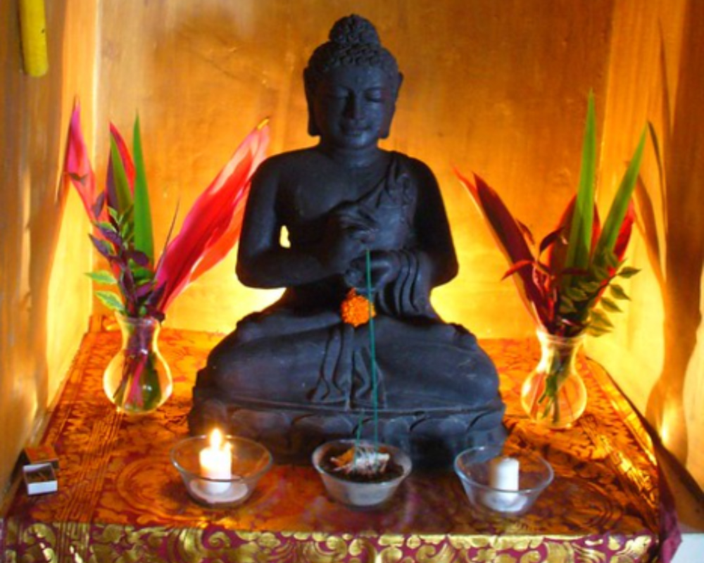 Spiritual shrine with Buddha statue, lit candles, and traditional Balinese offerings