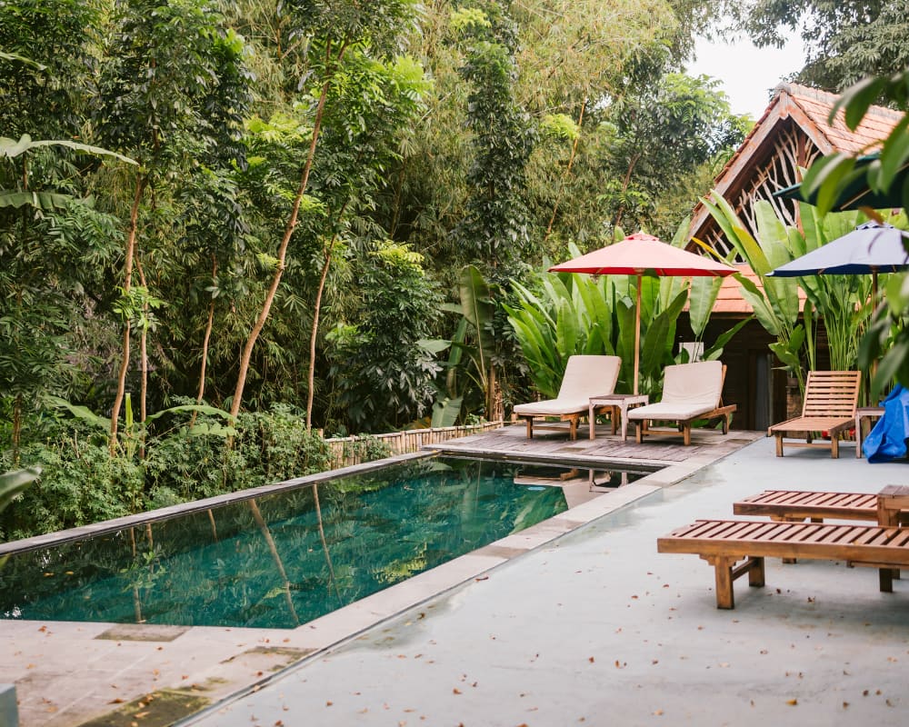 Relaxation spot by the pool in a serene Bali villa with greenery all around.