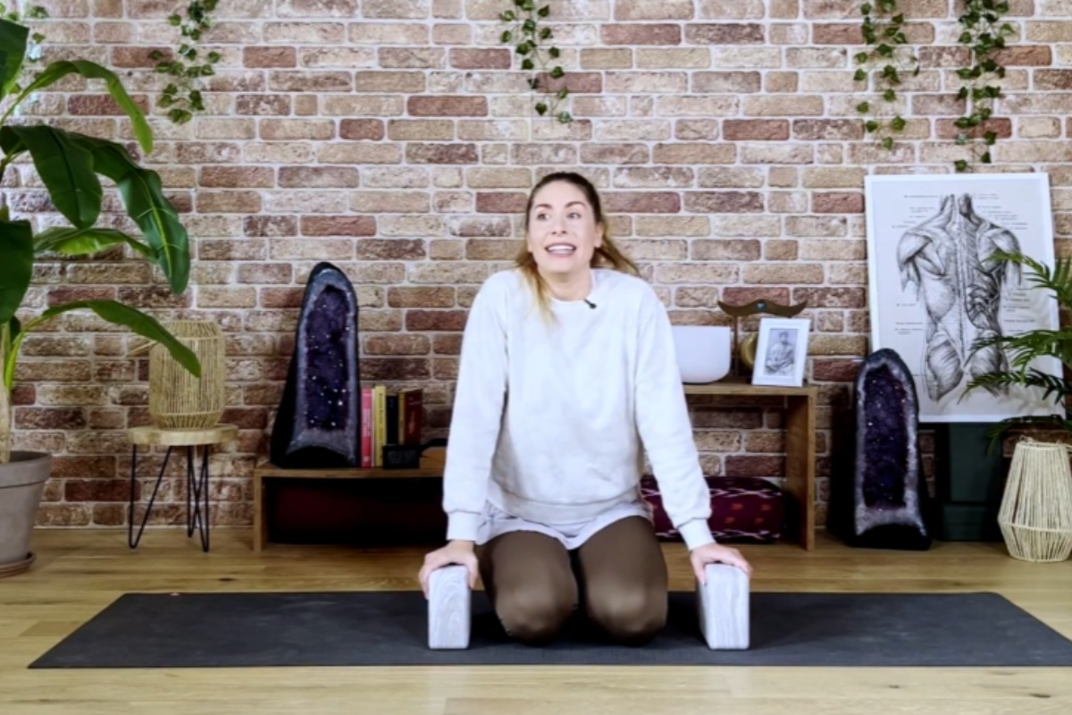 Yoga teacher seated on mat holding blocks preparing for Bhujapidasana arm balance