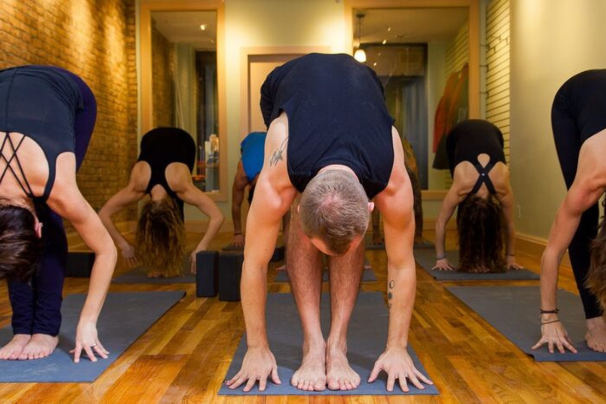 Students practicing a forward fold in a warm, wood-floored class at Brooklyn Yoga Project in Carroll Gardens.
