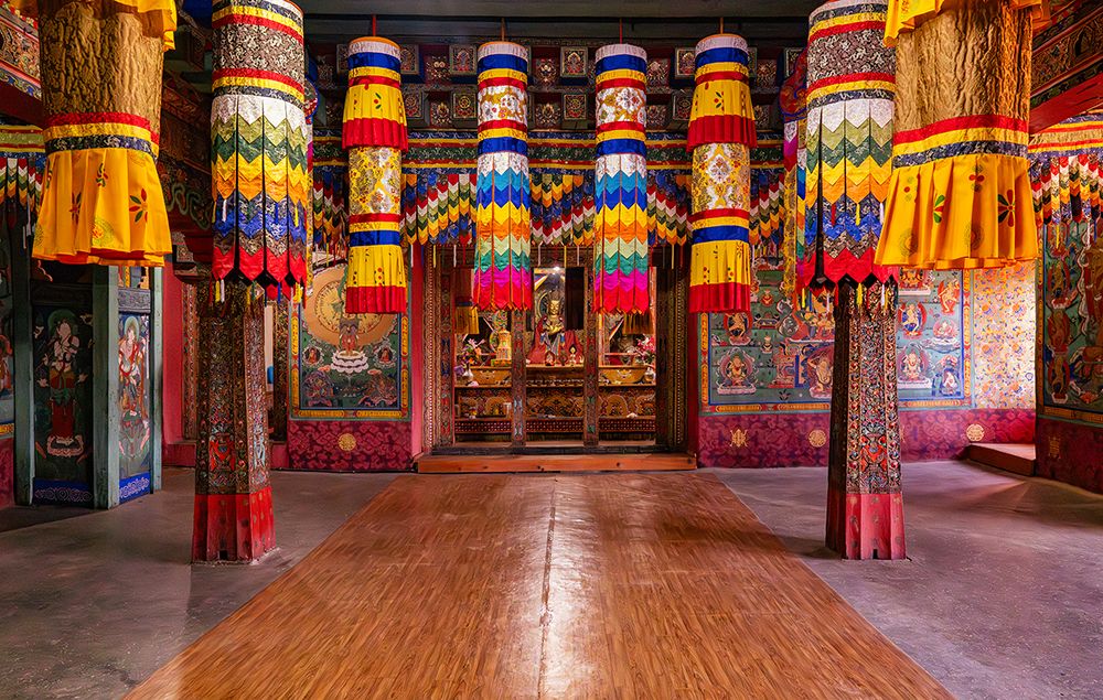 Interior of a colorful Buddhist monastery in Bhutan with hanging banners, painted columns, and a central altar.
