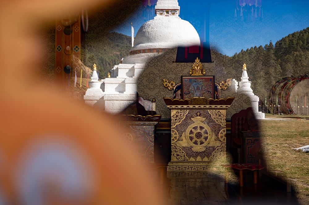 Layered view of a white stupa and a small temple in Bhutan, where monks perform daily rituals.