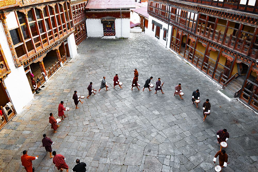 Monks and laymen practicing ritual movements with drums inside the main courtyard of a dzong in Bhutan.