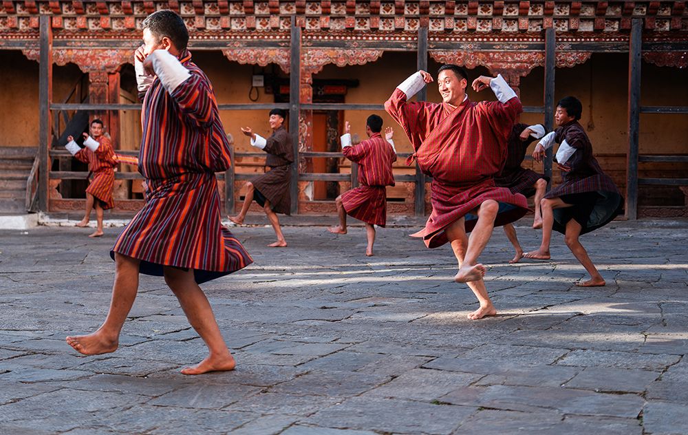 Bhutanese men performing a traditional folk dance inside a monastery courtyard in Bhutan, wearing striped gho garments.