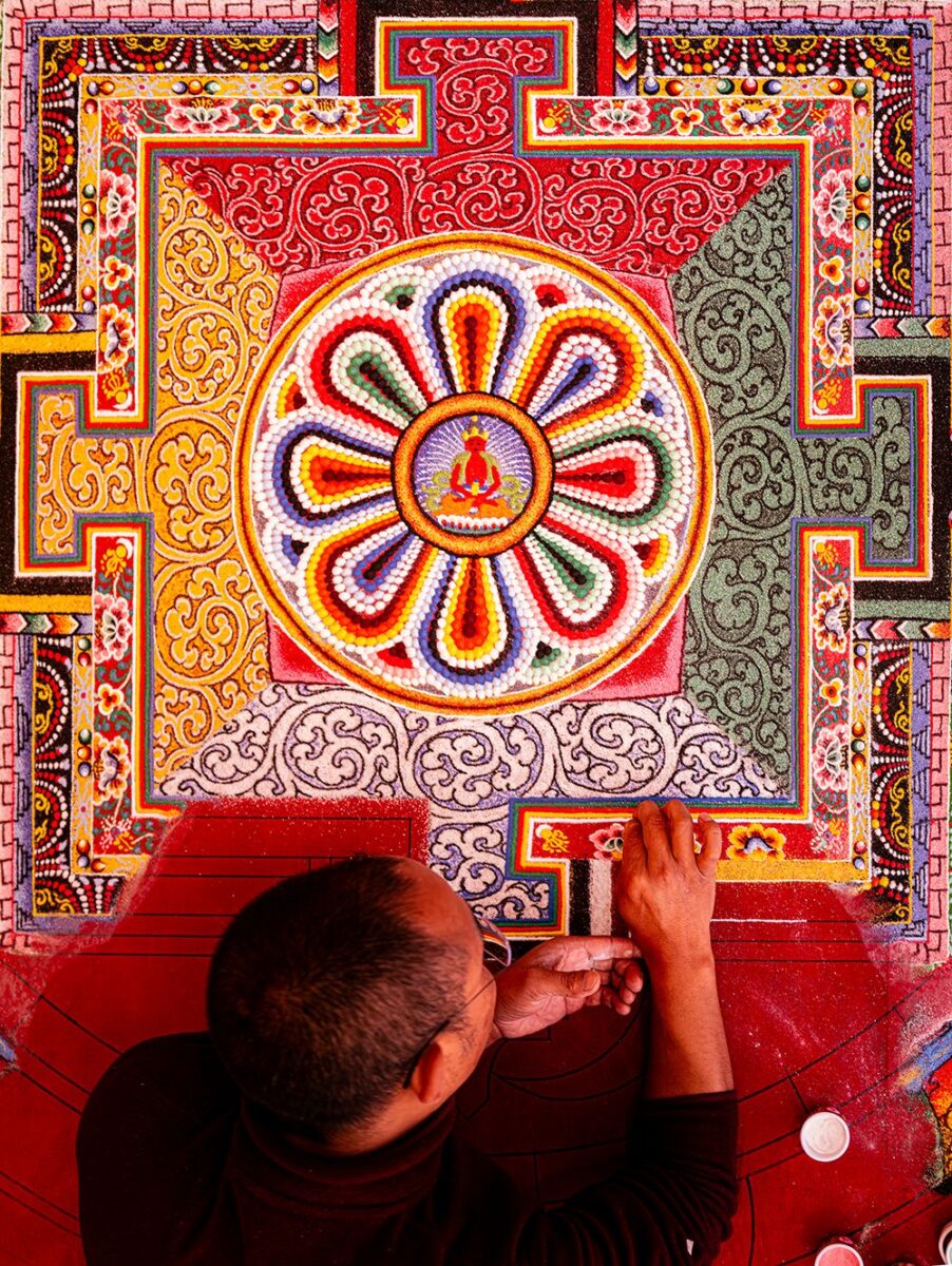 Bhutanese monk creating a colorful sand mandala inside a Buddhist monastery in Bhutan, photographed from above, showing intricate geometry and sacred ritual.