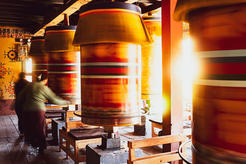 Row of spinning prayer wheels inside a Buddhist monastery in Bhutan, captured with motion blur as a monk turns them during a spiritual ritual.