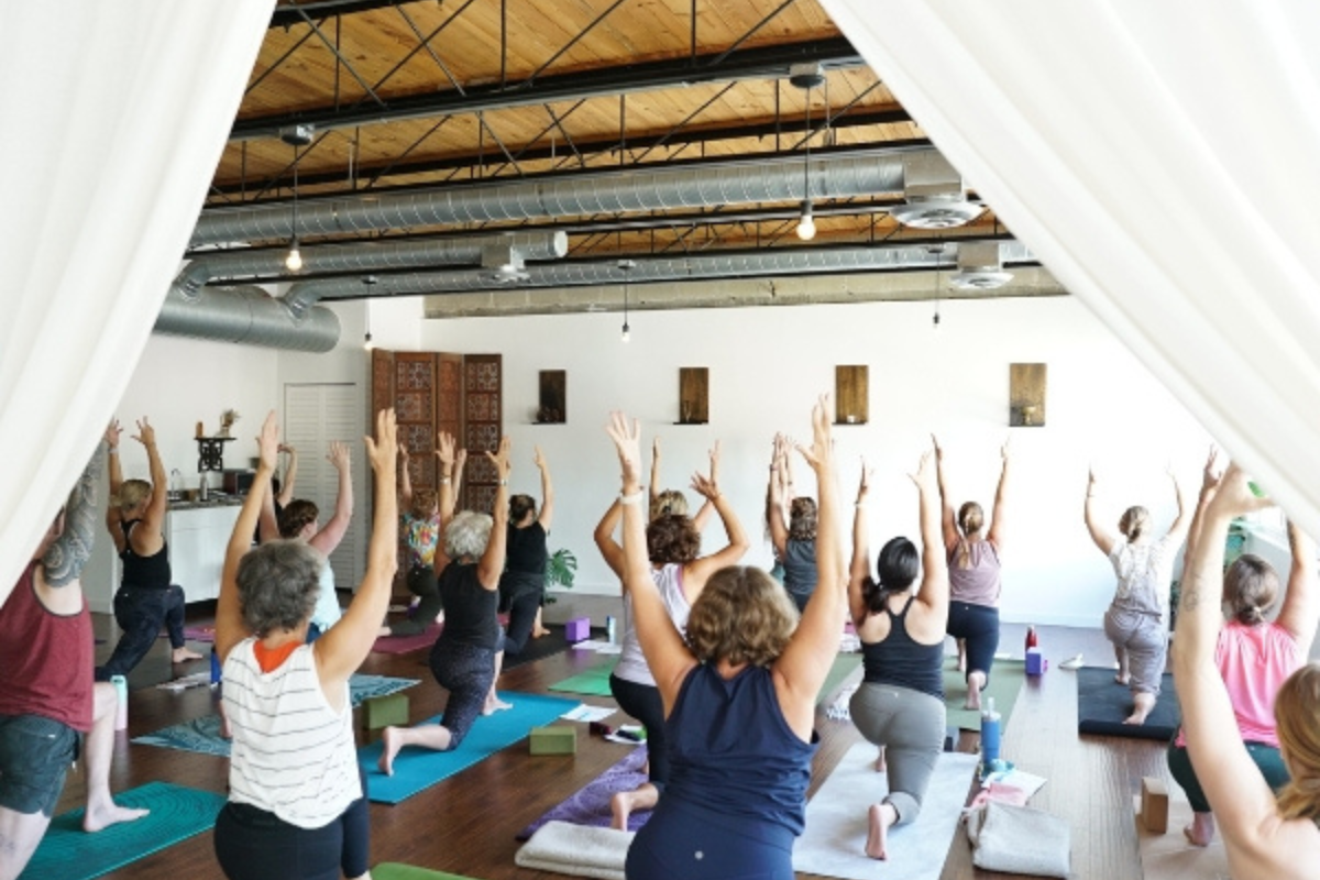 Group yoga class practicing a standing pose sequence in a light-filled yoga studio