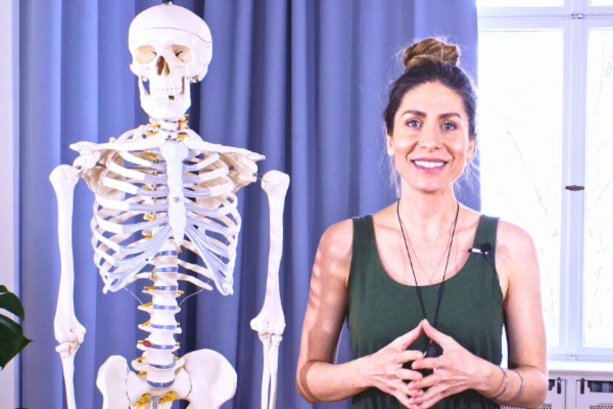 Yoga teacher explaining anatomy using a human skeleton model for alignment and movement education