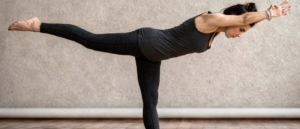 A yoga teacher is demonstrating the Warrior III pose from the side, with their body forming a straight line, arms reaching forward parallel to the floor. The standing leg is stable while the lifted leg extends back, showcasing balance and strength in this fierce warrior position.
