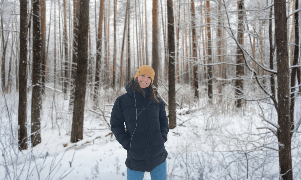A woman dressed in an aerogel puffer jacket, against a backdrop of a snowy forest.