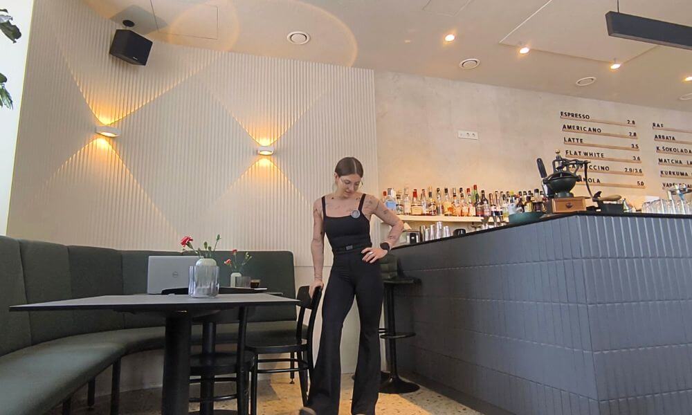 Woman in Graphene-X Kyorene Everywhere Jumpsuit styled with boots in a café setting for casual and travel outfit