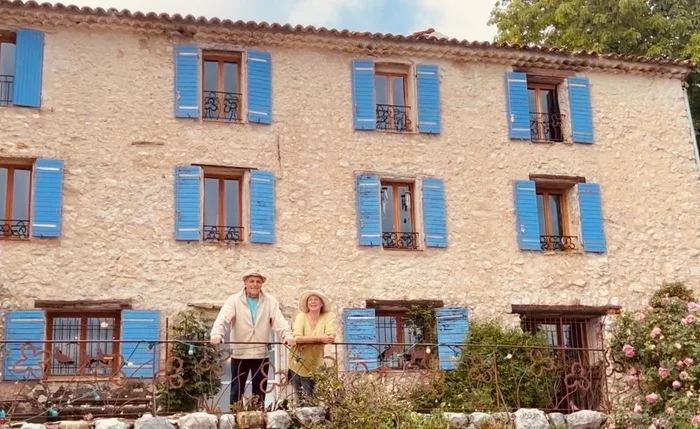 Berté et Carina posent devant la façade principale de la Ferme Saint Pierre à Bargème. La photo met en valeur l’architecture en pierre du domaine, ses volets bleus et l’atmosphère chaleureuse de cette ferme d’accueil du Haut Var.